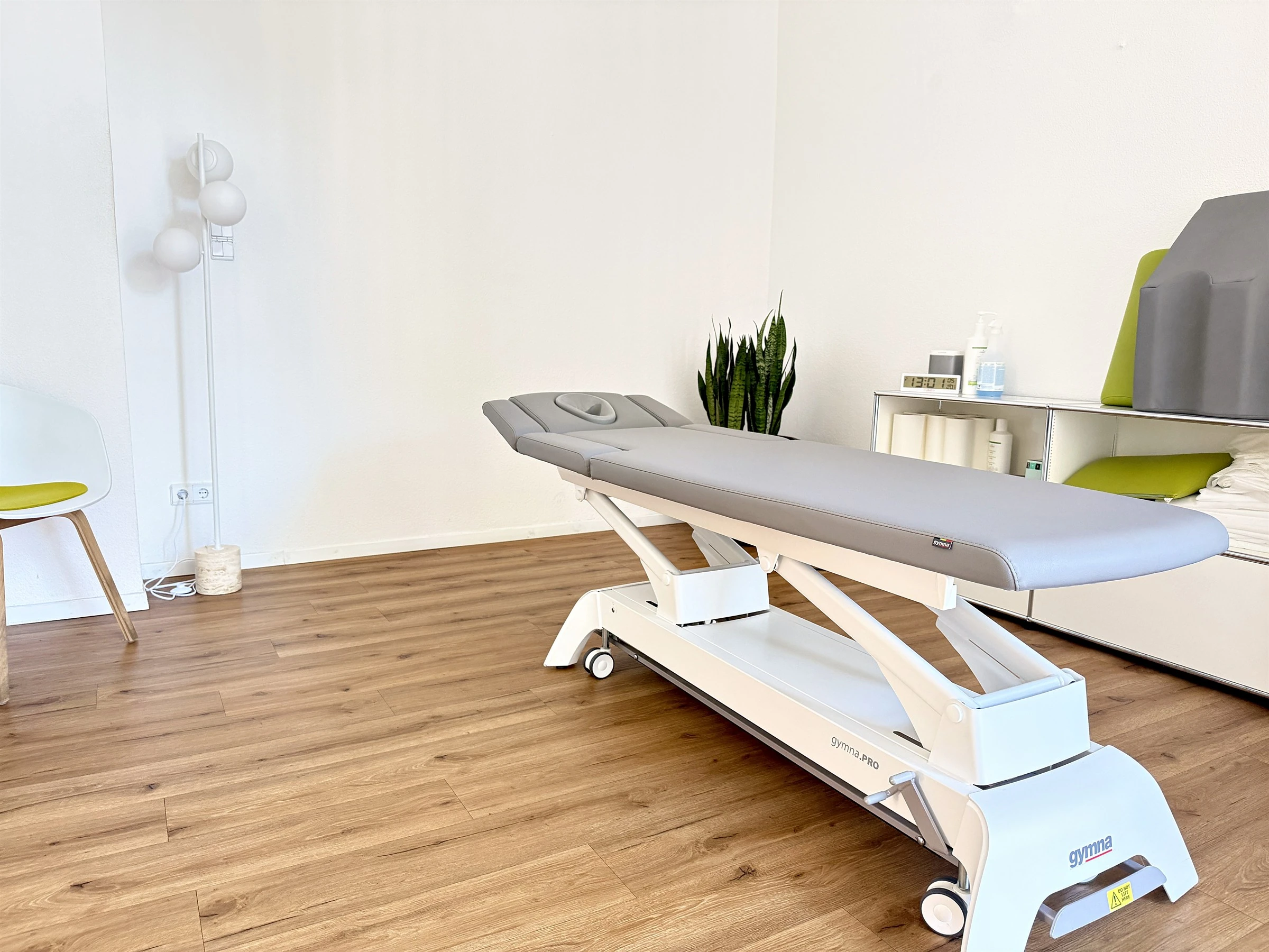 Heller Behandlungsraum mit grauer Therapieliege