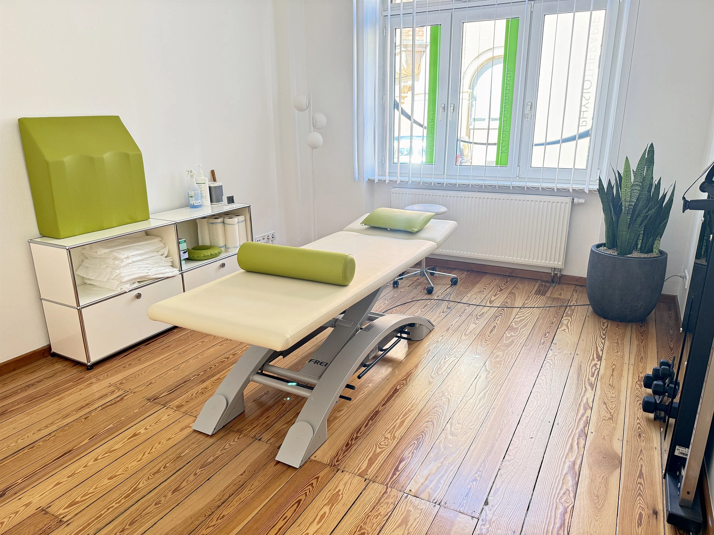 Heller Behandlungsraum mit Therapieliege und großem Fenster
