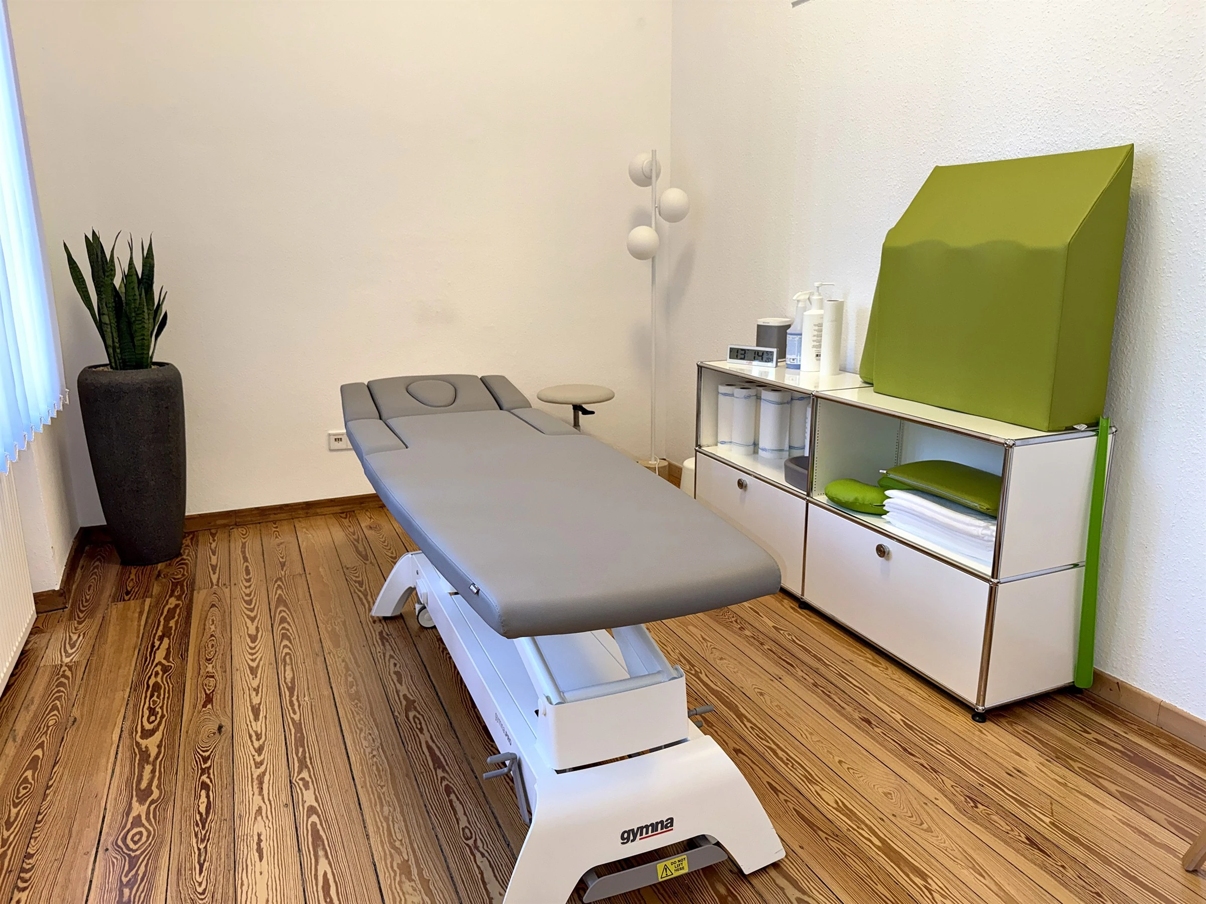 Ruhiger Behandlungsraum mit grauer Therapieliege